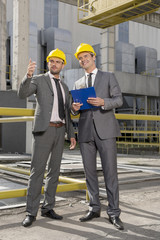 Full length of young male architects with clipboard discussing outside industry