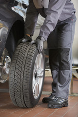 Low section of repairman fixing car's tire in workshop