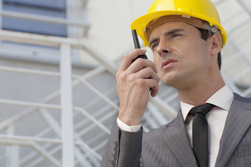Young male architect talking on two-way radio against building