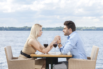 Young couple holding hands while looking at each other at outdoor restaurant by lake