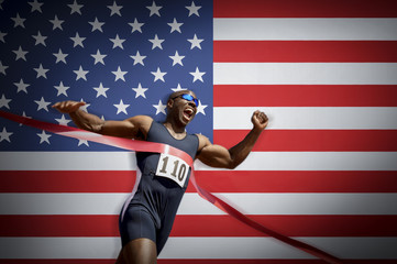 Male athlete crossing finish line against American flag