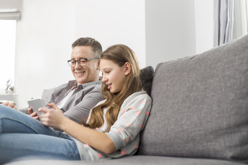 Obraz premium Father and daughter using digital tablet on sofa at home