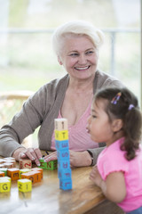 Happy grandmother looking away while granddaughter blowing stacked alphabet blocks in house