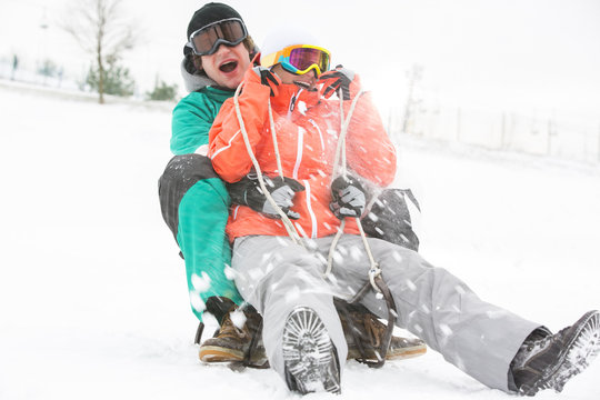 Excited young couple sledding in snow