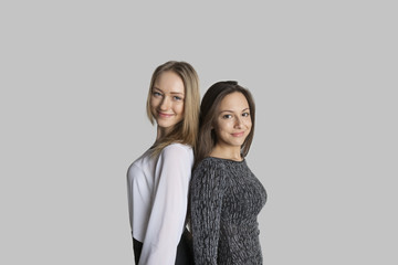 Portrait of smiling friends standing back to back against gray background