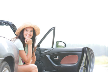 Happy woman sitting in convertible against clear sky