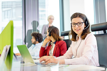 Portrait of smiling customer service representative using laptop while colleagues in background at office