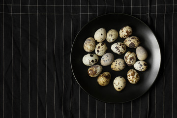 Quail eggs on black plate on black kitchen napkin background