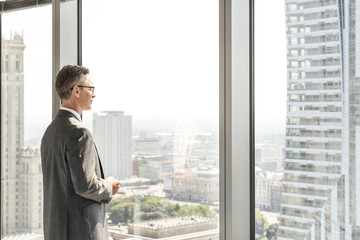 Fototapeta premium Side view of mature businessman looking through office window