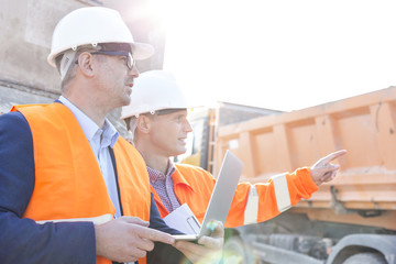 Supervisor showing something to colleague holding laptop at construction site