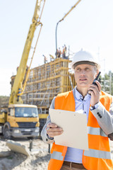 Male supervisor using walkie-talkie while holding clipboard at construction site