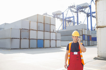 Mid adult man using walkie-talkie in shipping yard
