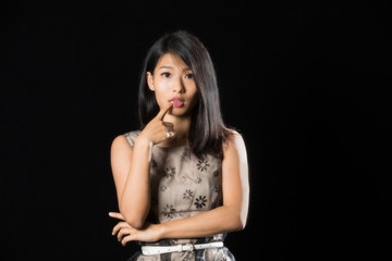 Pretty chinese girl with finger on her lip standing against black background