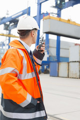 Middle-aged man using walkie-talkie in shipping yard