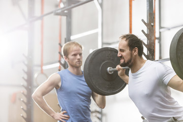 Man assisting friend in lifting barbell at crossfit gym