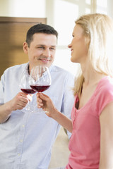 Happy couple toasting red wine glasses in kitchen
