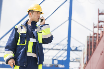 Mid adult male worker using walkie-talkie in shipping yard