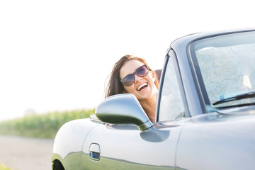 Excited woman enjoying road trip in convertible against clear sky