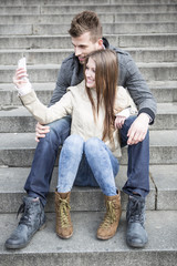 Full length of young couple taking picture of themselves while sitting on steps outdoors