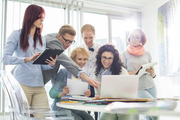 Smiling creative businesspeople working on laptop at desk in office