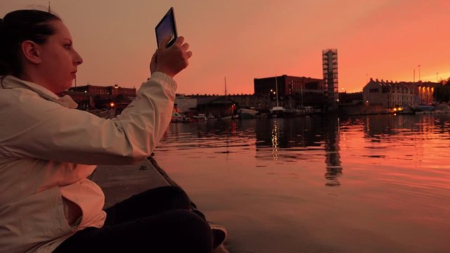making photos with a tablet computer at the sunset: woman on the riverside