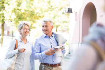 Obraz premium Happy middle-aged couple with map walking in city
