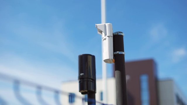 System of video surveillance and motion sensors are located on the corner of the fence close-up. Modern equipment for the protection of the territory from outsiders. Buildings on the background.