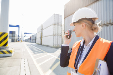 Female engineer using walkie-talkie in shipping yard - obrazy, fototapety, plakaty