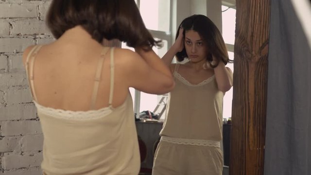 Woman looking in the big mirror. Young lady stands in bedroom wearing in pajamas shorts and top nude color. Happy girls in the morning.