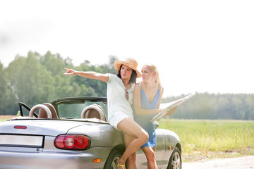 Woman showing something to friend with map while leaning on convertible