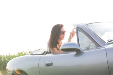 Woman reading map in convertible against clear sky on sunny day
