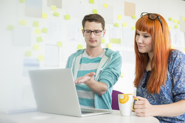 Businessman showing something to female colleague on laptop in creative office