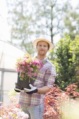 Portrait of gardener holding flower pot outside greenhouse