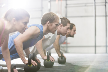 Dedicated people doing pushups with kettlebells at crossfit gym