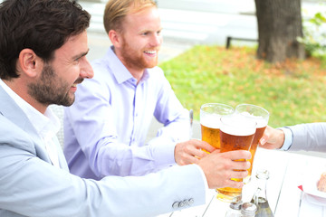 Fototapeta na wymiar Businessmen toasting beer glasses with female colleague at outdoor restaurant