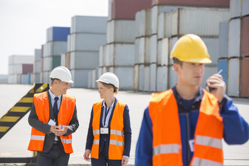 Worker using walkie-talkie while colleagues discussing in shipping yard