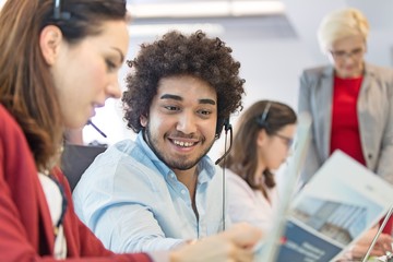 Young businessman discussing with businesswoman with colleagues in background at office