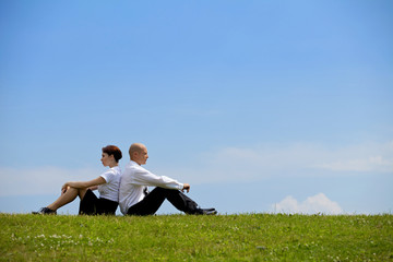 Business couple sitting back to back on grass