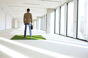 Full length rear view of young businessman standing on turf in empty office