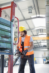 Young male worker pushing hand truck in metal industry