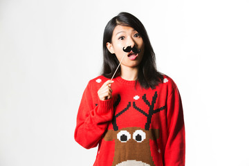 Portrait of woman in Christmas sweater standing with fake moustache