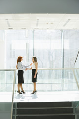 Fototapeta na wymiar Full-length of businesswomen shaking hands at office hallway