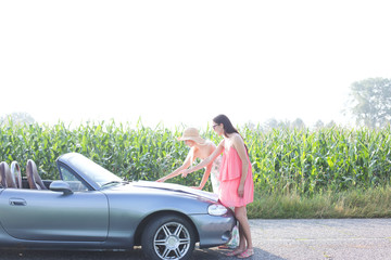 Female friends reading map on convertible against clear sky