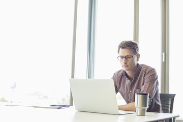 Mid-adult businessman using laptop at desk in creative office