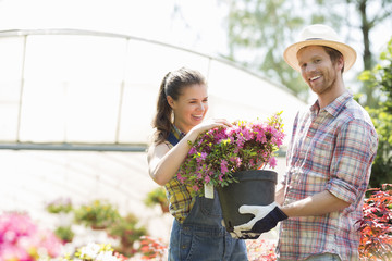 Happy gardeners holding flower pot outside greenhouse