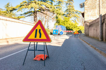 Road sign lane narrowing. In background site of road work.
