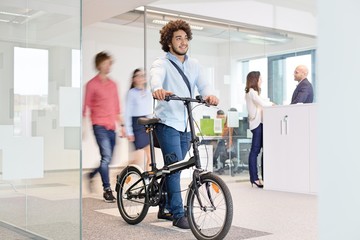 Young businessman walking with bicycle while colleagues in background at office