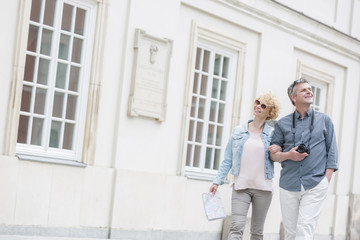 Fototapeta premium Happy middle-aged tourist couple walking arm in arm by building