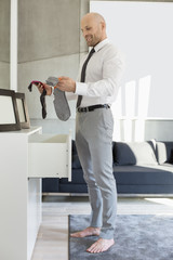 Full length side view of businessman selecting socks at home