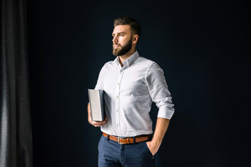 Young bearded businessman, dressed in a white shirt standing near the window on the background of a...